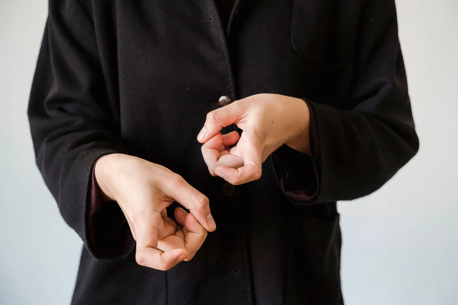 A person in a black jacket displaying a hand gesture, possibly sign language.